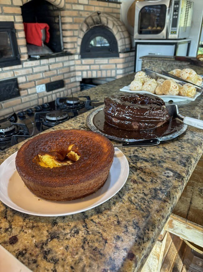 Bolos caseiros e pão de queijo com forno a lenha ao fundo